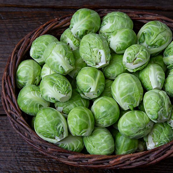 Fresh green Brussels sprouts overflowing a woven basket on a dark wooden table.