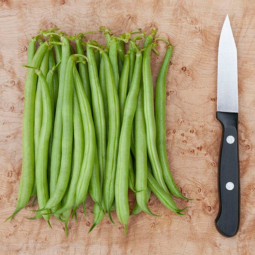 Fresh green beans and paring knife on a wood cutting board, ready for healthy cooking prep.