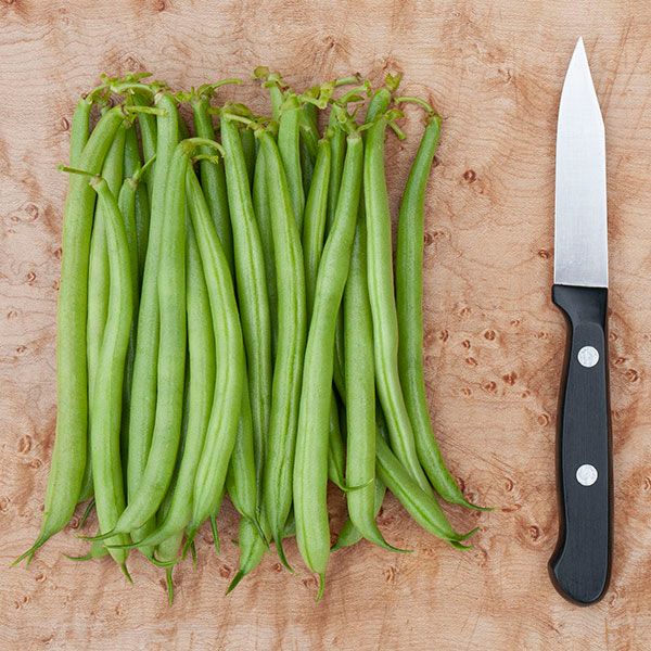 Fresh green beans and paring knife on a wood cutting board, ready for healthy cooking prep.