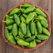 Fresh, spicy green jalapeño peppers in a rustic basket on a wooden table.