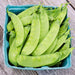 Fresh green snow peas in a blue market basket on rustic wood.