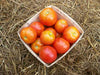 Fresh ripe red tomatoes in a wooden basket on straw. Garden harvest produce.