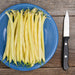 Golden wax beans on a blue plate with a knife on a rustic wooden background. Fresh harvest.