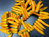 Numerous bright yellow chili peppers scattered on a dark surface. Fresh, vibrant hot peppers for cooking.