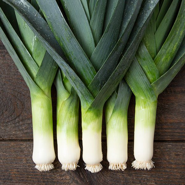 Five fresh leeks with vibrant green leaves and crisp white stalks on a rustic wooden surface.