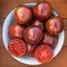 Bowl of vibrant striped heirloom tomatoes, deep red with green streaks. Two sliced tomatoes reveal juicy, seed-filled interiors. Fresh garden harvest.