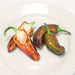 Fresh dark brown & green chili peppers on white plate; one sliced showing seeds & red interior.