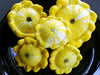 Five fresh yellow variegated summer pattypan squash on a dark plate.