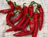 Fresh, vibrant red chili peppers with green stems on a white textured cloth. Spicy cooking ingredient.