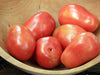 Six ripe red Roma tomatoes in a rustic wooden bowl. Fresh plum tomatoes for cooking or sauces.