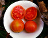 Ripe orange-red tomatoes: two whole, two sliced revealing red flesh, in a white bowl. Fresh garden produce.