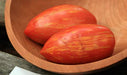 Vibrant red and orange striped Roma tomatoes in a rustic wooden bowl.