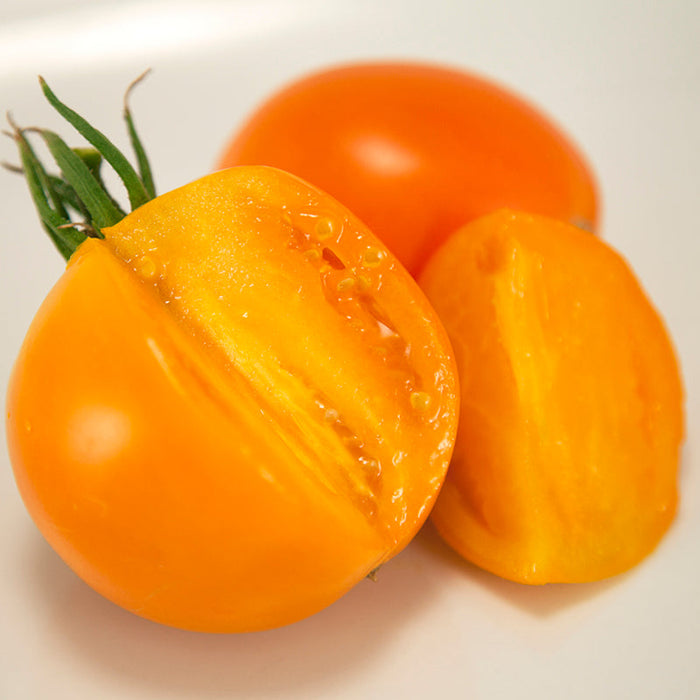 Three fresh orange-yellow tomatoes, one halved with a green stem, showing juicy pulp and seeds.