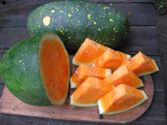 Orange-fleshed watermelon with spotted green rind, sliced on a wooden board.