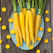 Vibrant yellow carrots with green tops on a blue plate, surrounded by carrot slices on a wooden background. Fresh garden harvest.